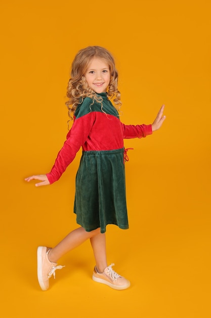 Beautiful little blonde girl in a velour red and green dress on a yellow background