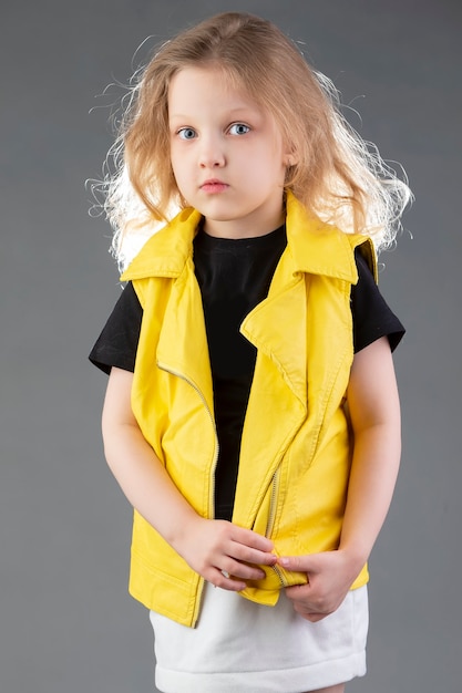 Photo beautiful little blonde girl in a yellow jacket on a gray background