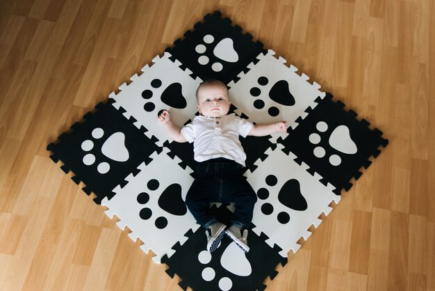 Foto un bellissimo bambino giace su un tappeto in via di sviluppo, un gioco di puzzle in bianco e nero con un'espressione dolce