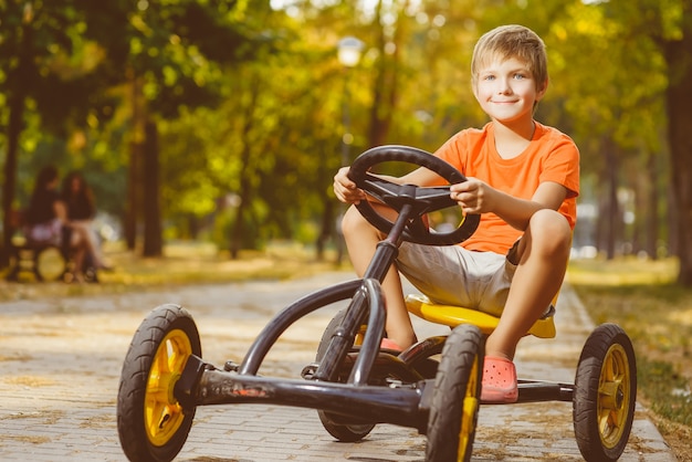Красивый маленький мальчик на игрушечной машине в летнем городском парке