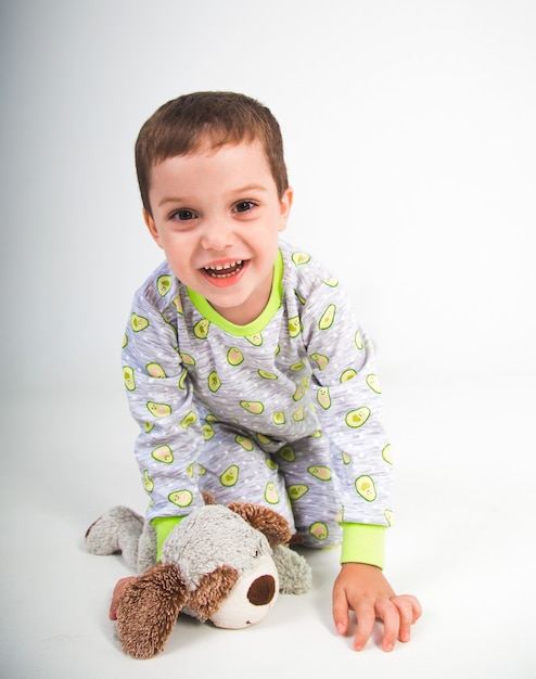 A beautiful little boy smiles in pajamas with a toy on a white background