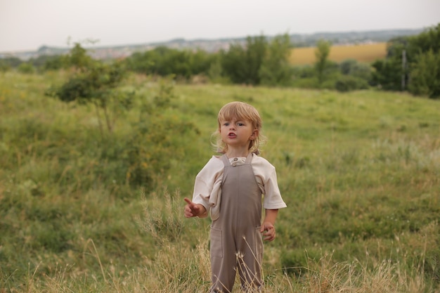 a beautiful little boy with blond hair and curly hair is resting in nature by the river