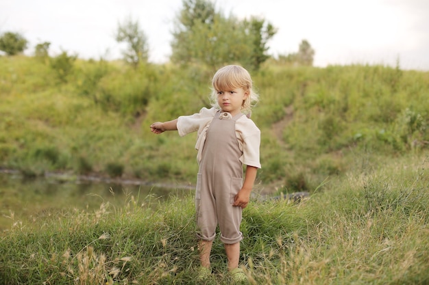 a beautiful little boy with blond hair and curly hair is resting in nature by the river