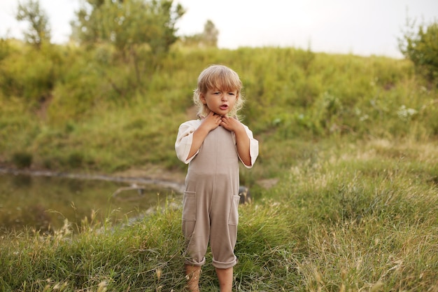 a beautiful little boy with blond hair and curly hair is resting in nature by the river