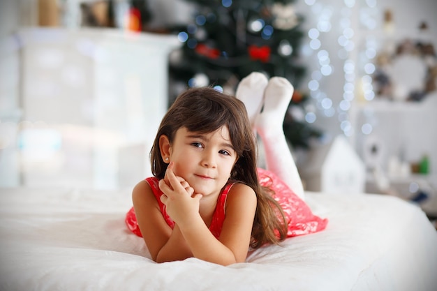 Bella piccola ragazza castana che aspetta un miracolo nelle decorazioni di natale