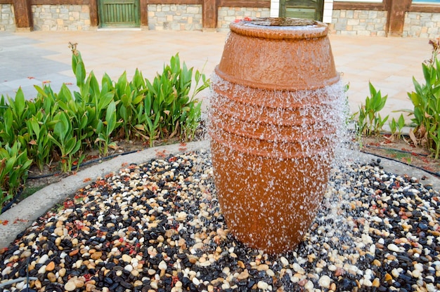 A beautiful little fountain in the form of a brown vase a jug with falling drops of water on colored