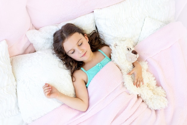 テディベアとベッドで寝ている5-6歳の美しい少女