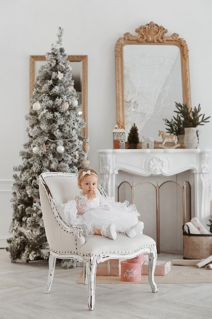 Beautiful little girl in an amazing dress sitting near the Christmas tree. Christmas miracles. Happy New Year