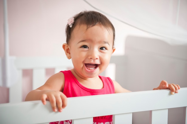 Красивая маленькая девочка азиатской внешности улыбается и играет в кроватке