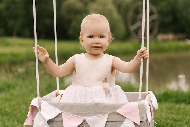 A beautiful little girl in a basket with a balloon and a cake celebrates her first birthday