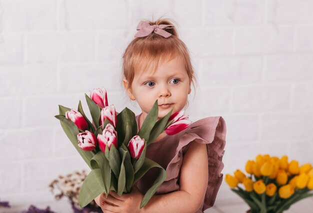 Beautiful little girl in a beautiful dress with a bouquet of flowers in a light studio