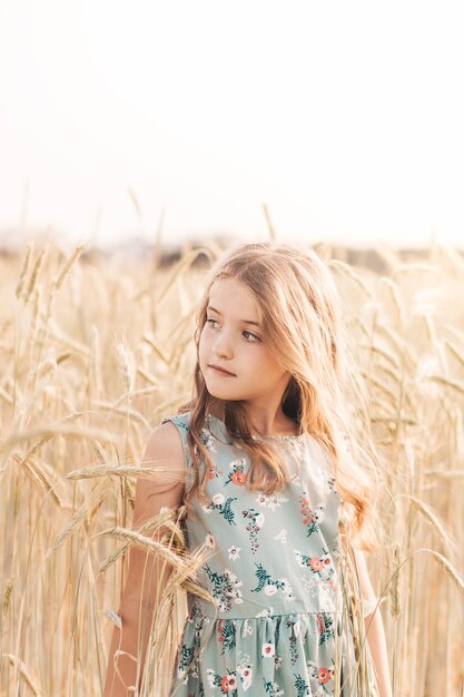 Bella bambina bionda con i capelli lunghi che cammina attraverso un campo di grano