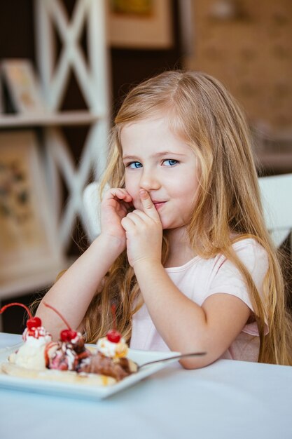 Beautiful little girl blonde woman smiling in cafe eats a dessert ice cream with fruits