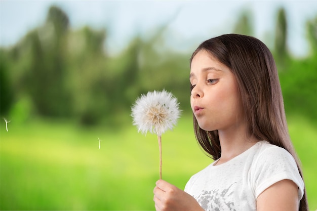 Bella bambina che soffia il dente di leone su sfondo naturale sfocato verde