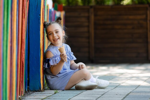 Beautiful little girl in blue dress eating ice cream in park colorful background