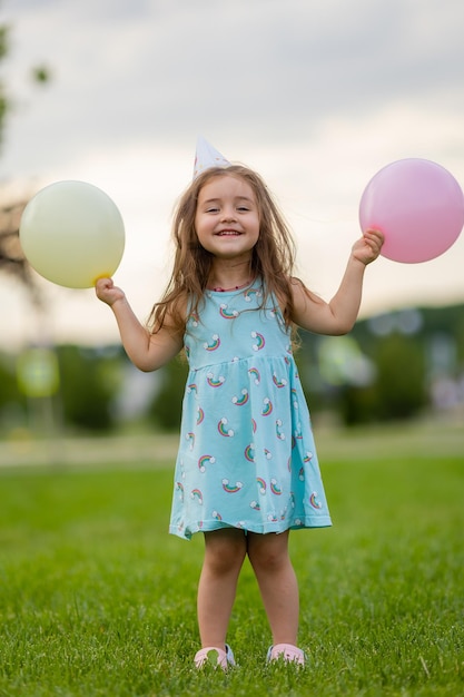 公園のお誕生日おめでとうの風船と青いドレスと帽子の美しい少女