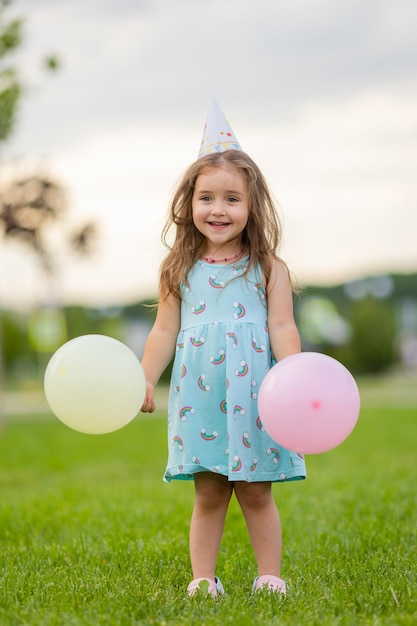 Beautiful little girl in blue dress and hat with balloons in park happy birthday