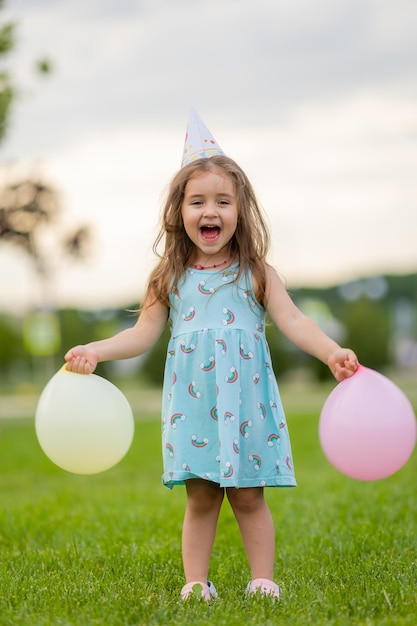 公園のお誕生日おめでとうの風船と青いドレスと帽子の美しい少女