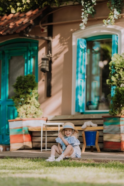 красивая маленькая девочка в синем платье, соломенной шляпе и солнцезащитных очках, играющая на открытом воздухе, синий фон, карта