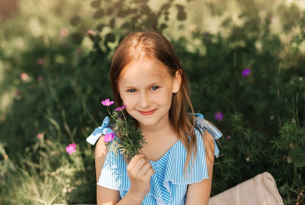 Bella bambina in un vestito blu con fiori in natura in estate