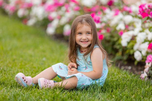 Beautiful Little girl in blue dress with flowers in park summertime