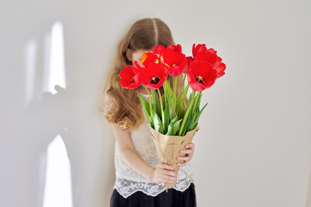 Beautiful little girl child with bouquet of red tulips