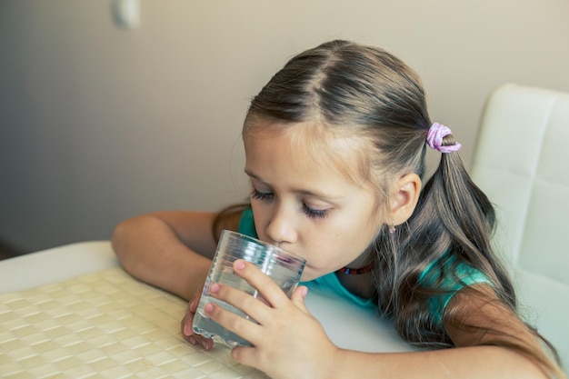 Beautiful little girl drinks clean water from a transparent glass