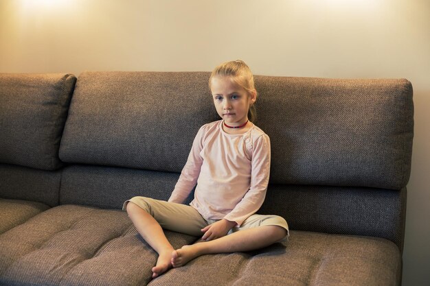 Beautiful little girl eating unhealthy food while watching tv at the sofa