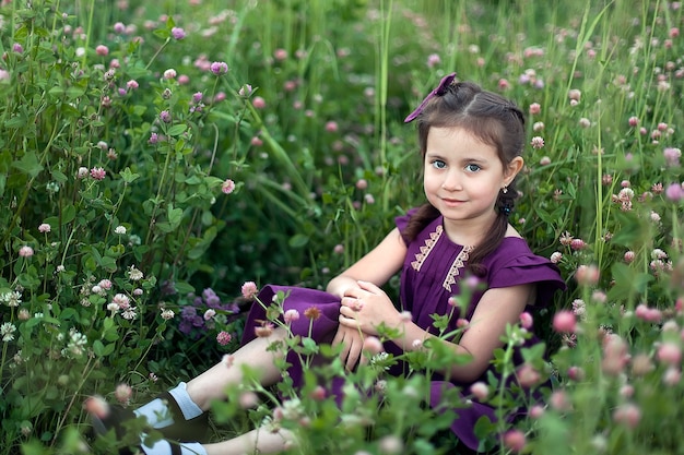 Beautiful little girl in a field among flowers and green grass.