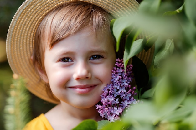 Beautiful little girl in a hat near lilac flowers