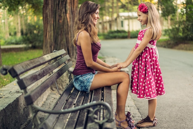 Beautiful little girl and her mother at bench in the park.