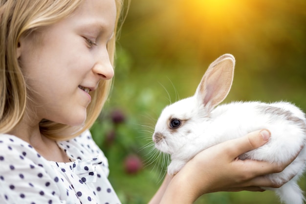 Beautiful little girl holding in hands white rabbit at the garden