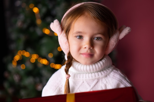 写真 プレゼントやクリスマスツリーのボケライトの近くに座っている帽子の美しい少女