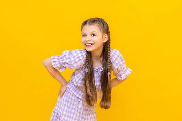 Photo a beautiful little girl is smiling happily a young girl posing in a summer suit a happy joyful child on a yellow isolated background