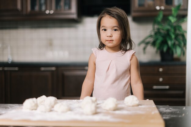 Beautiful little girl is standing by the sliced pieces of dough and looks at the camera