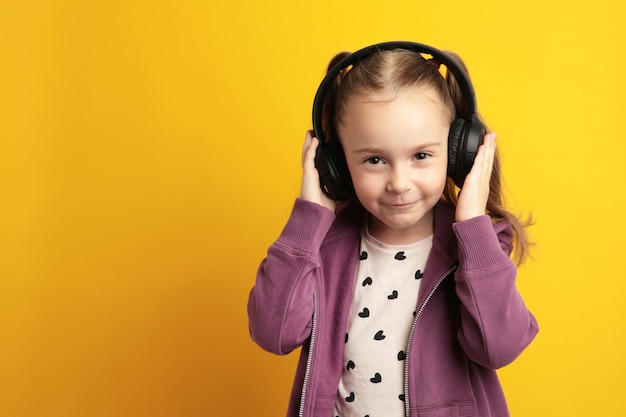 Beautiful little girl listening to music on yellow background Top view