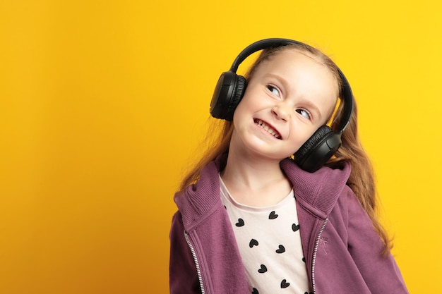 Beautiful little girl listening to music on yellow background top view