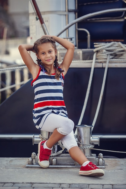 Una bellissima bambina in stile marinaro sullo sfondo di barche e yacht.