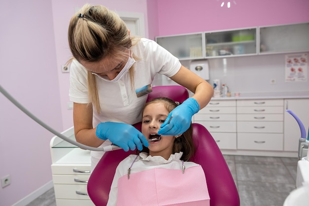 아름다운 작은 소녀가 여성 치과 의사의 치과 치료 중에 입을 넓게 열고 있습니다.