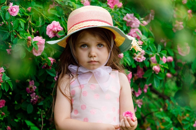 분홍색 드레스를 입은 아름다운 소녀와 장미가 있는 정원의 모자. 고품질 사진