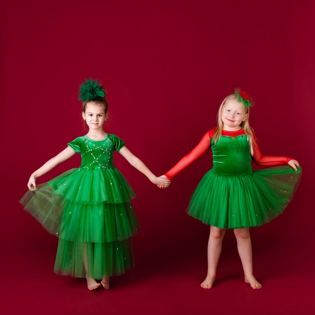 Beautiful little girl princesses dancing in luxury green dress isolated on red wall. Carnival party with costumes