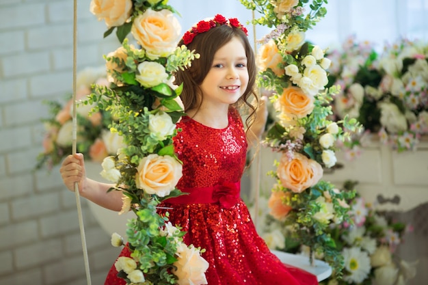 Bella bambina in vestito rosso che si siede su un'altalena con decorazioni floreali