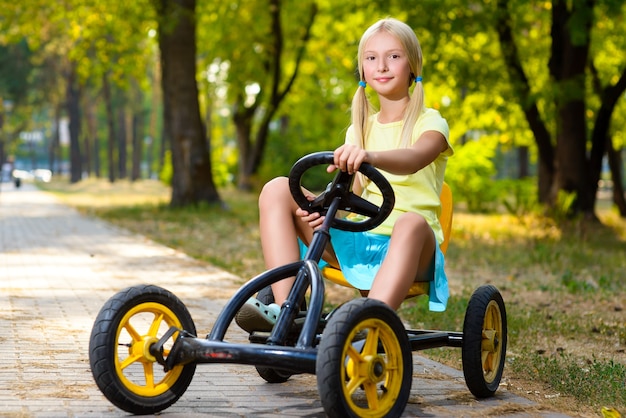 Beautiful little girl riding toy car in summer city park