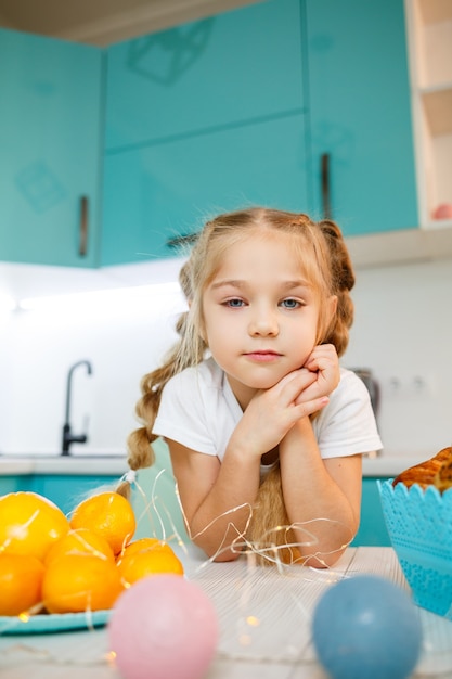 Красивая маленькая девочка семи лет. сидит за столом на кухне. Одет в белую футболку. Счастье и радость на детском лице