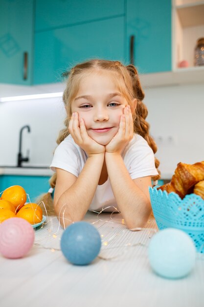 Beautiful little girl of seven years old. sitting at the table in the kitchen. Dressed in a white T-shirt. Happiness and joy on a child's face