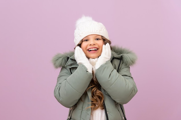 Photo a beautiful little girl shows joy that winter has come. child is very happy with good and warm winter clothes of good quality. baby in a warm jacket and a knitted hat.