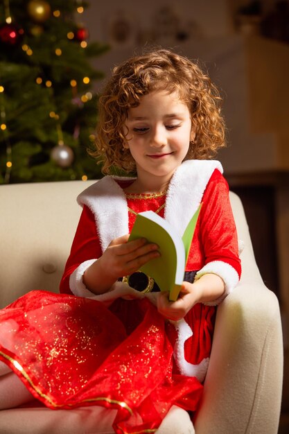 Beautiful little girl sits on the chair next to a nicely decorated christmas tree