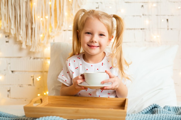 beautiful little girl sitting on the bed with a cup of tea