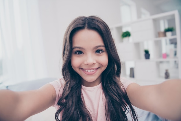 Beautiful little girl sitting on her bed with a smartphone