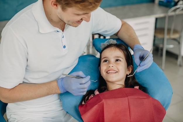 Photo beautiful little girl sitting in stomatology chair looking at her dentist smiling before doing a teeth surgery